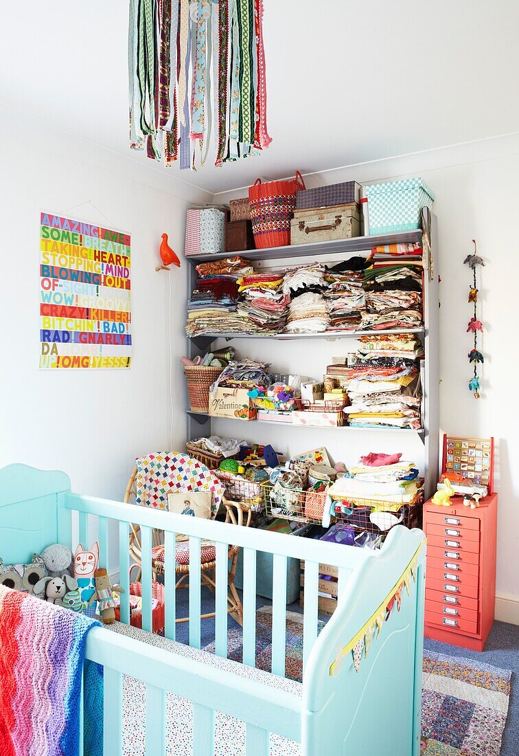 Clothes folded on shelf in child's nursery with turquoise painted cot,  London family home,  England,  UK