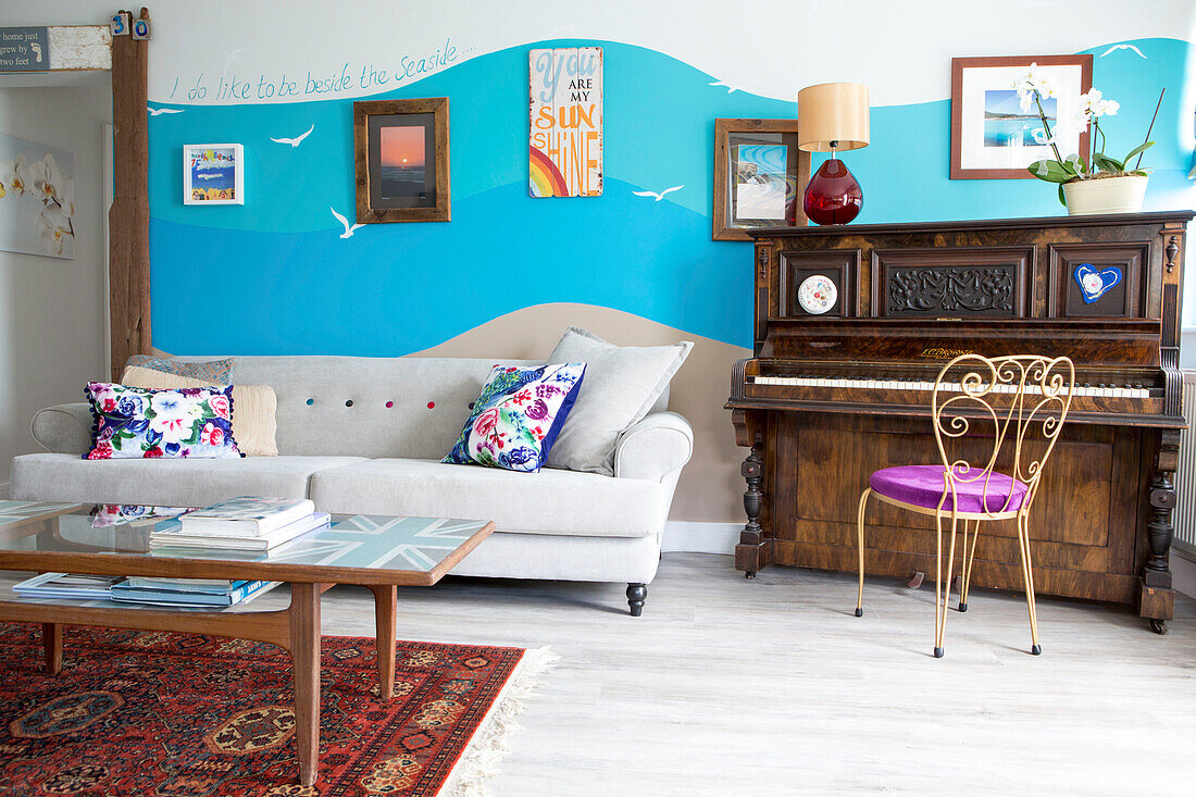 Artwork on beach themed wall with piano and sofa in renovated 1950s coastal beach house West Sussex UK
