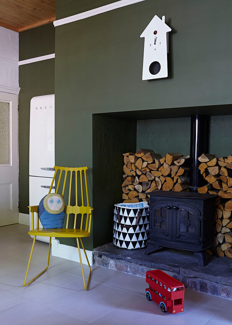 Wood burner recessed to green wall of London family home with yellow chair and toy bus,  England,  UK