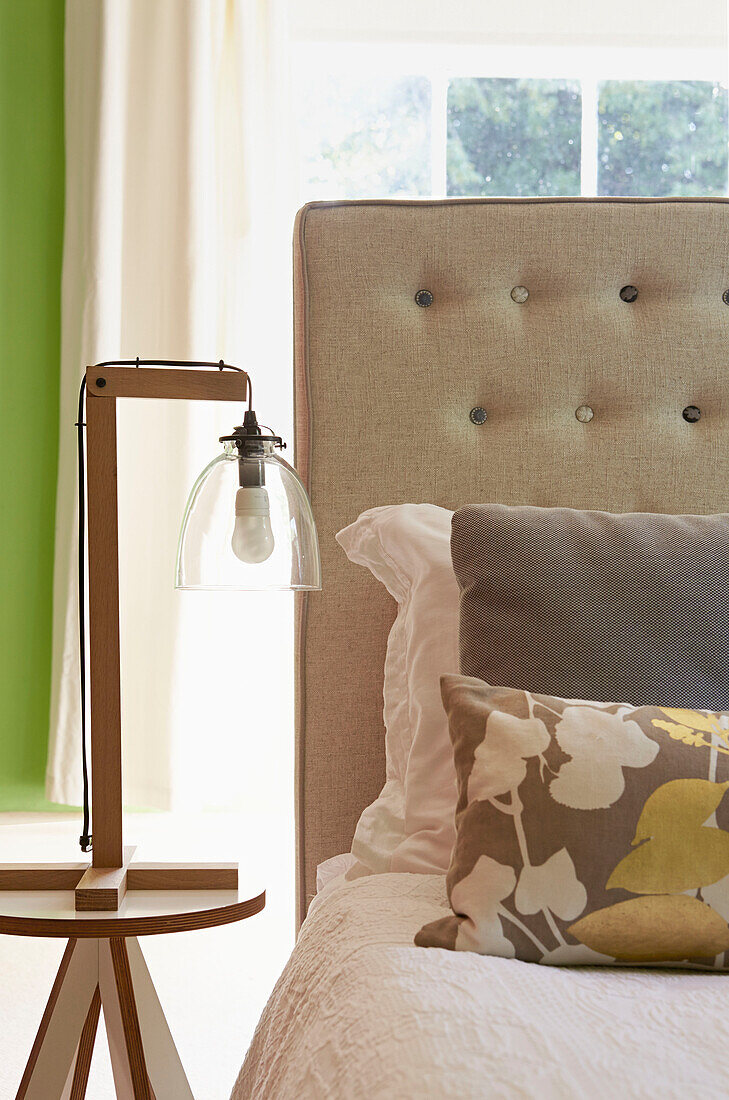 Lamp with clear shade at bedside of bed with buttoned headboard in London home,  England,  UK