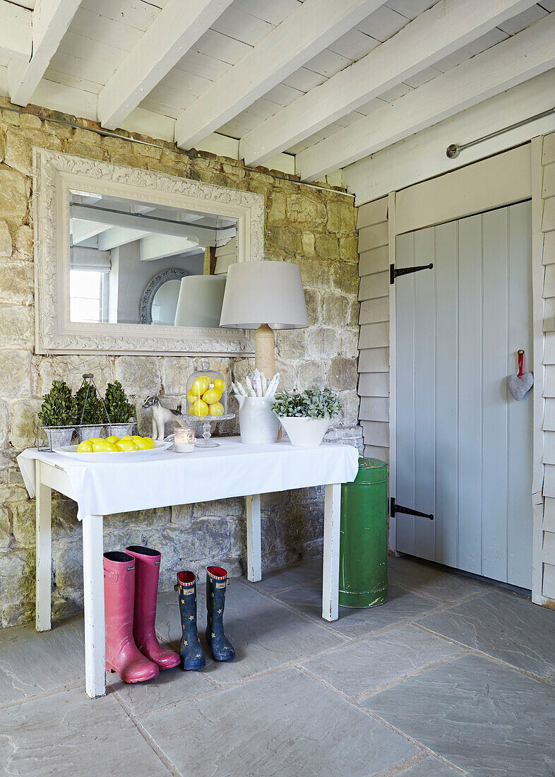 Rectangular mirror above table with wellington boots in flagstone entrance hallway of UK farmhouse