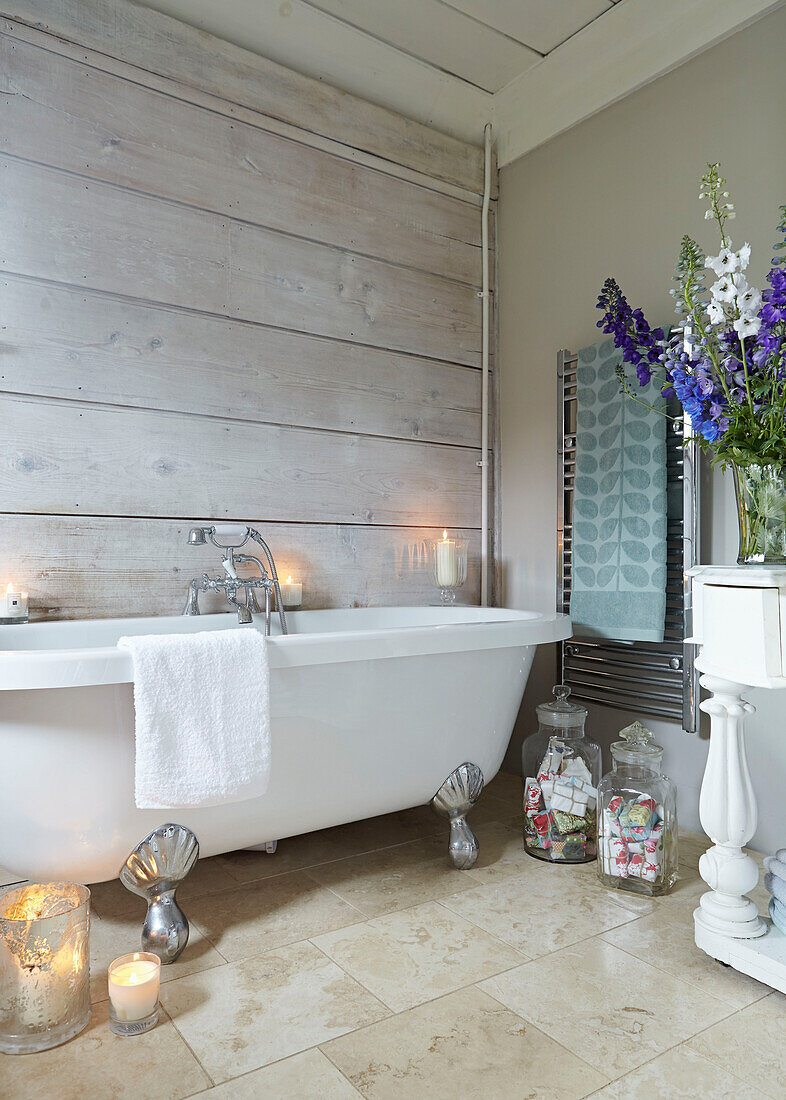 Weiße freistehende Badewanne mit Handtuch auf verchromtem Heizkörper im getäfelten Badezimmer eines britischen Bauernhauses
