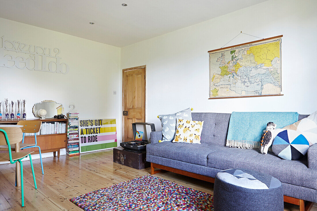 Graues Sofa mit Wandkarte und hölzernem Sideboard im Wohnzimmer eines Londoner Einfamilienhauses, England, UK
