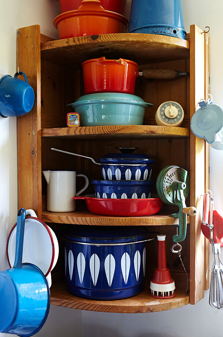 Bright saucepans and cake tin on wooden wall mounted corner shelf in Brabourne farmhouse kitchen,  Kent,  UK