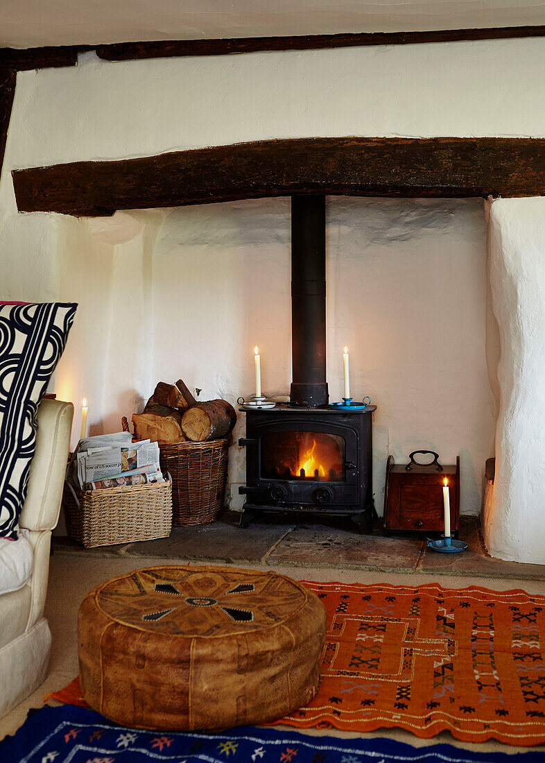 Brown leather footstool at candlelit fireplace with wood burning stove in Brabourne farmhouse,  Kent,  UK