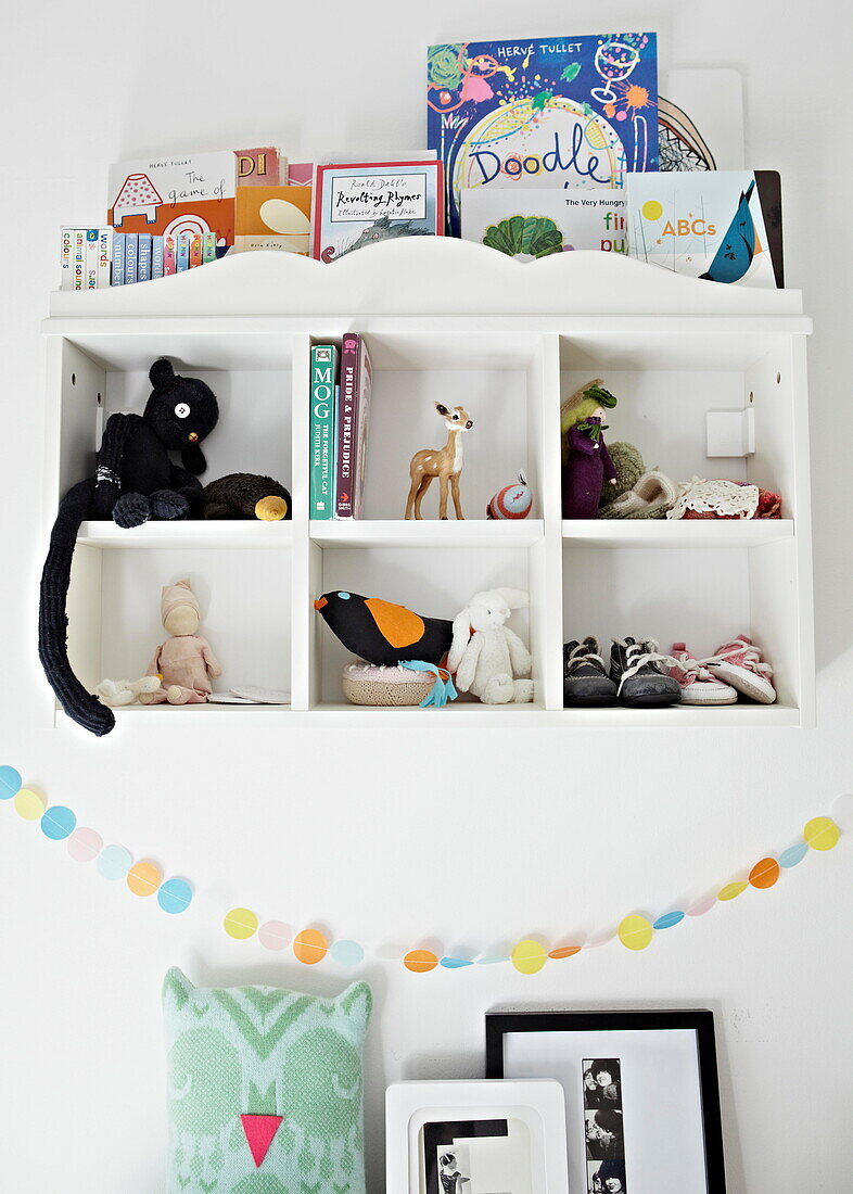 Soft toys and books on wall mounted shelving in child's room in London family home  England  UK