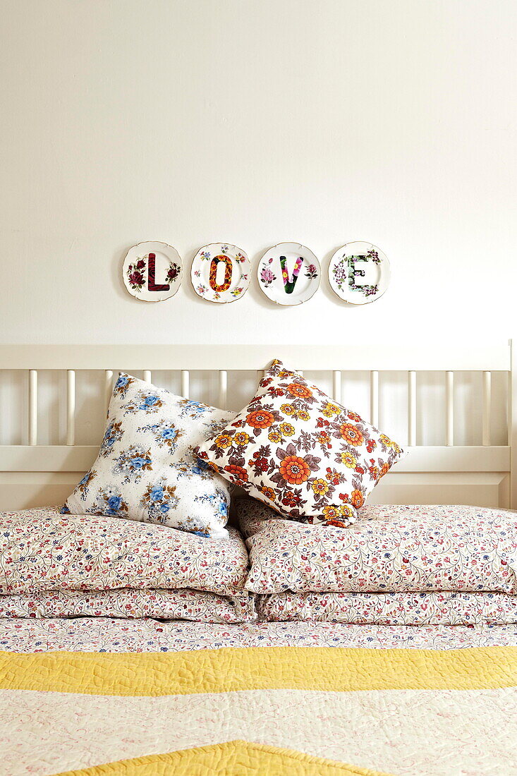 Einzelnes Wort 'LOVE' auf dekorativen Tellern über floral gemusterten Kissen im Schlafzimmer eines Hauses in Birmingham England UK
