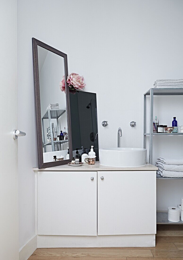 Wash basin and mirror with shelving unit in white bathroom of contemporary London home   England   UK