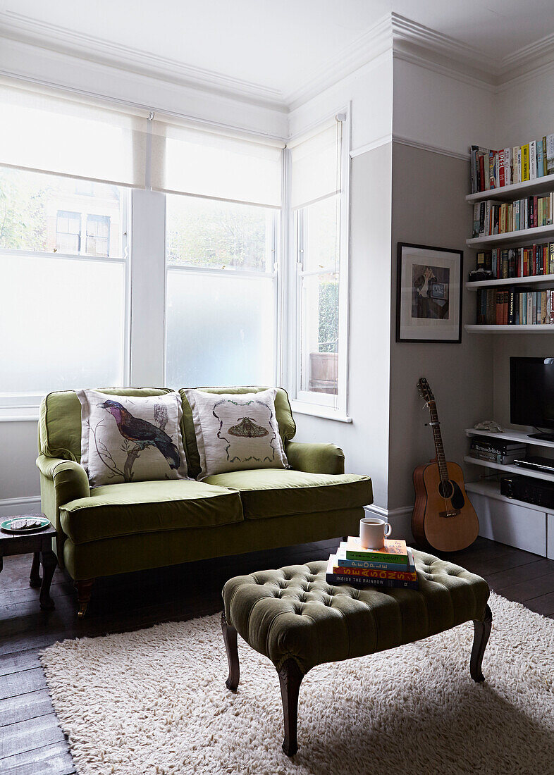 Bücher auf Ottomane mit grünem Sofa im Erker eines modernen Hauses in London England UK