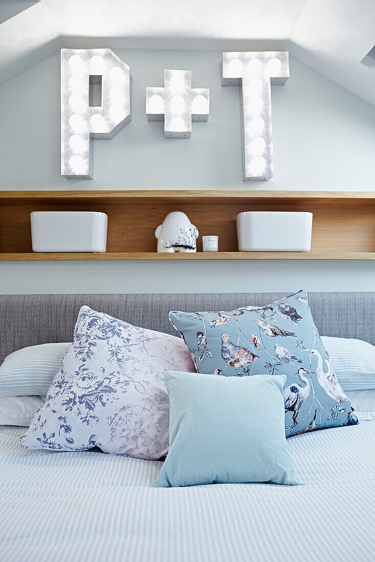Bird patterned cushion on double bed below wooden shelf with letters 'P' and 'T' of London townhouse  England  UK