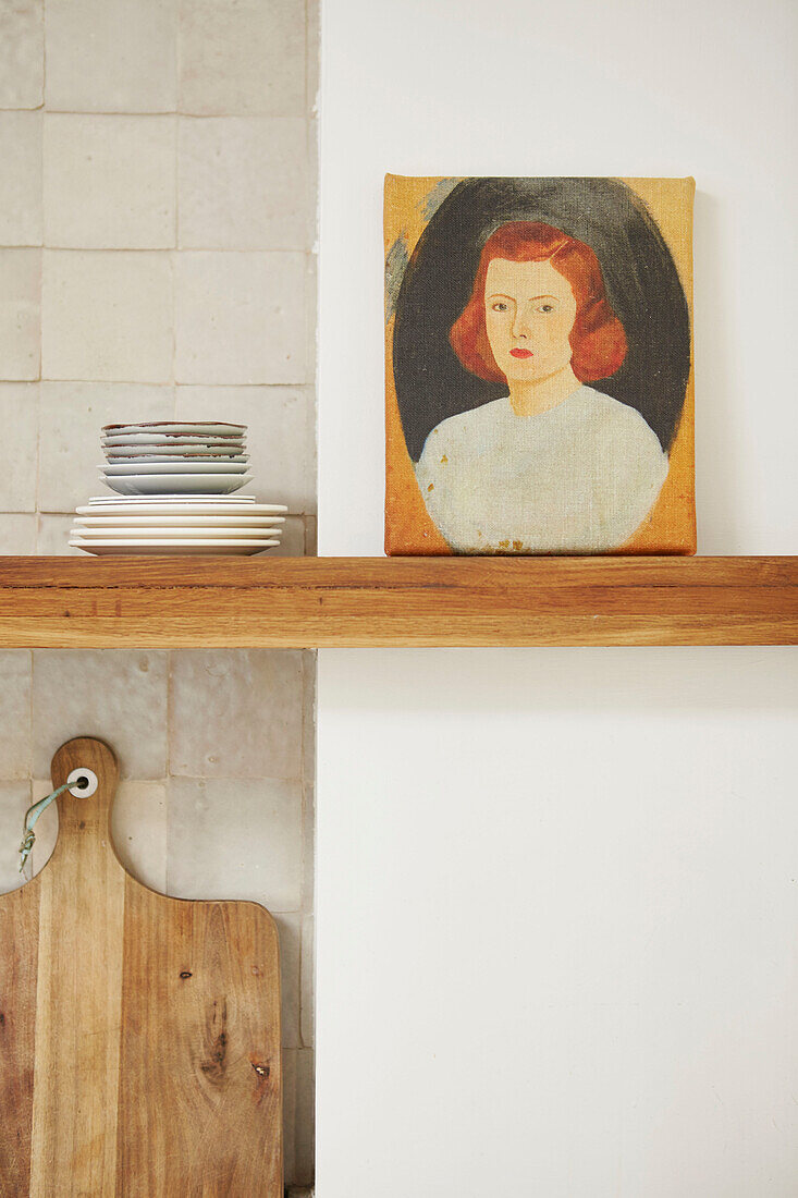 Portraiture on shelf with side plates and chopping board in kitchen of London home  UK