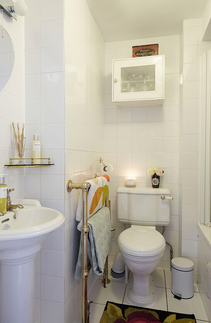 Bath towels hang on brass rack in white tiled bathroom of Faversham home,  Kent,  UK