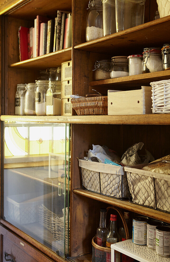 Storage jars and books on wooden shelving with glass  panel in West Yorkshire kitchen  UK