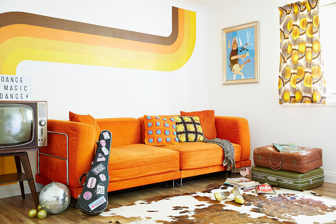 Orangefarbenes Sofa mit Vintage-Koffern in einem Wohnzimmer im Retrostil in einem Haus in East Riding of Yorkshire, England UK