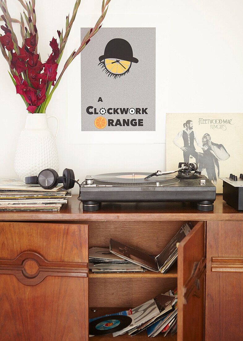 Schallplattensammlung und Lilien mit Uhr auf hölzernem Sideboard in einer Londoner Wohnung UK