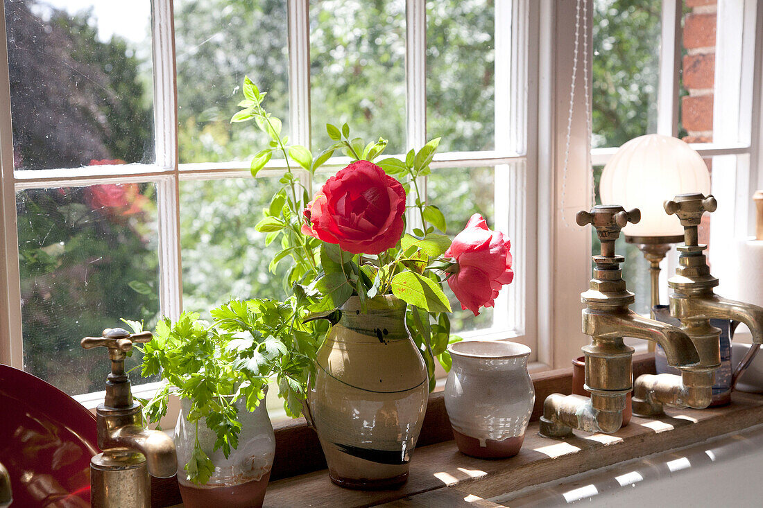 Vase mit Blumen und alten Wasserhähnen auf der Fensterbank einer umgebauten Wassermühle