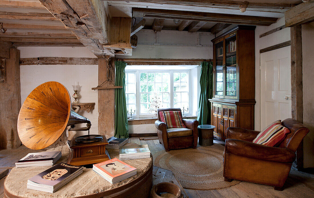 Gramophone and books on table with matching brown leather chairs in watermill conversion 