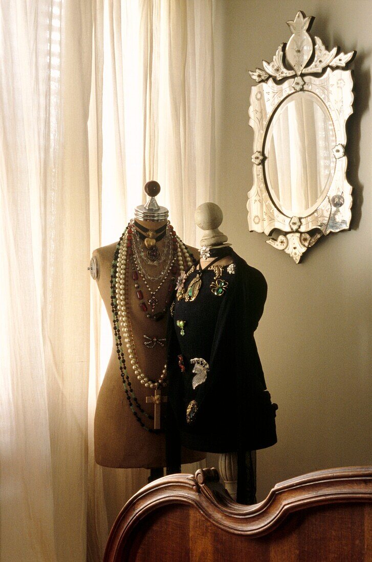 Two tailors mannequins covered with vintage jewellery and shawls in bedroom