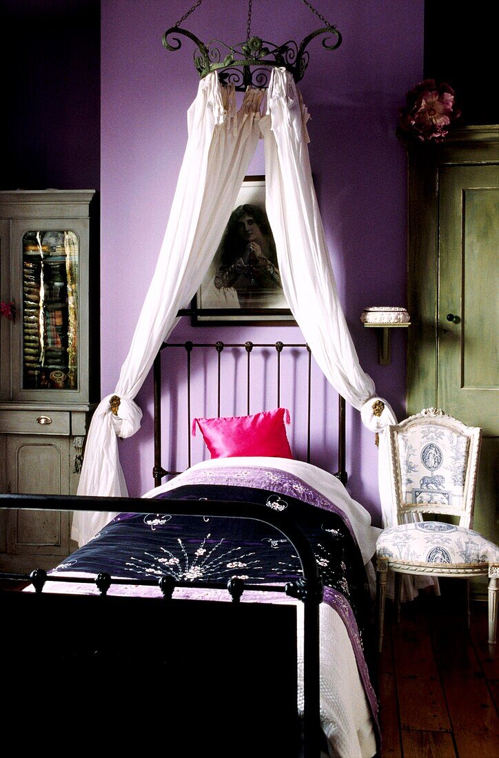 Fliederfarbenes Mädchenzimmer mit gusseisernem Einzelbett und Metallkronleuchter mit Musselinvorhängen