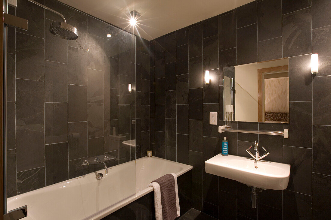 Dark travertine tiled bathroom with white bath and basin