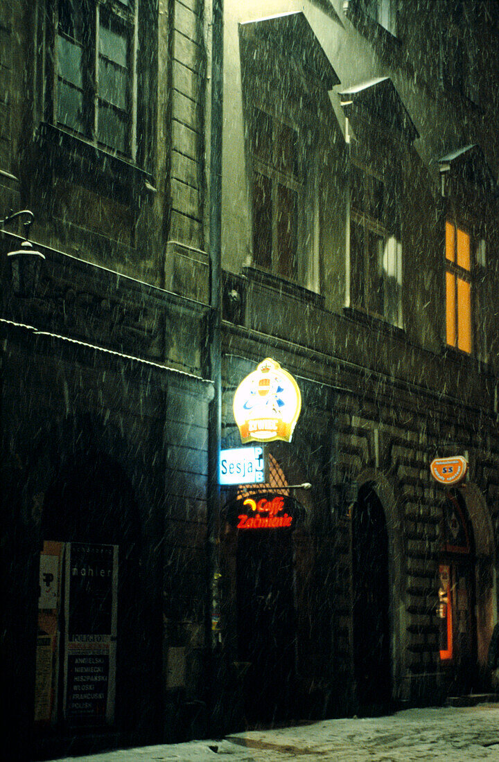 Snow falling in street by bar at night 
