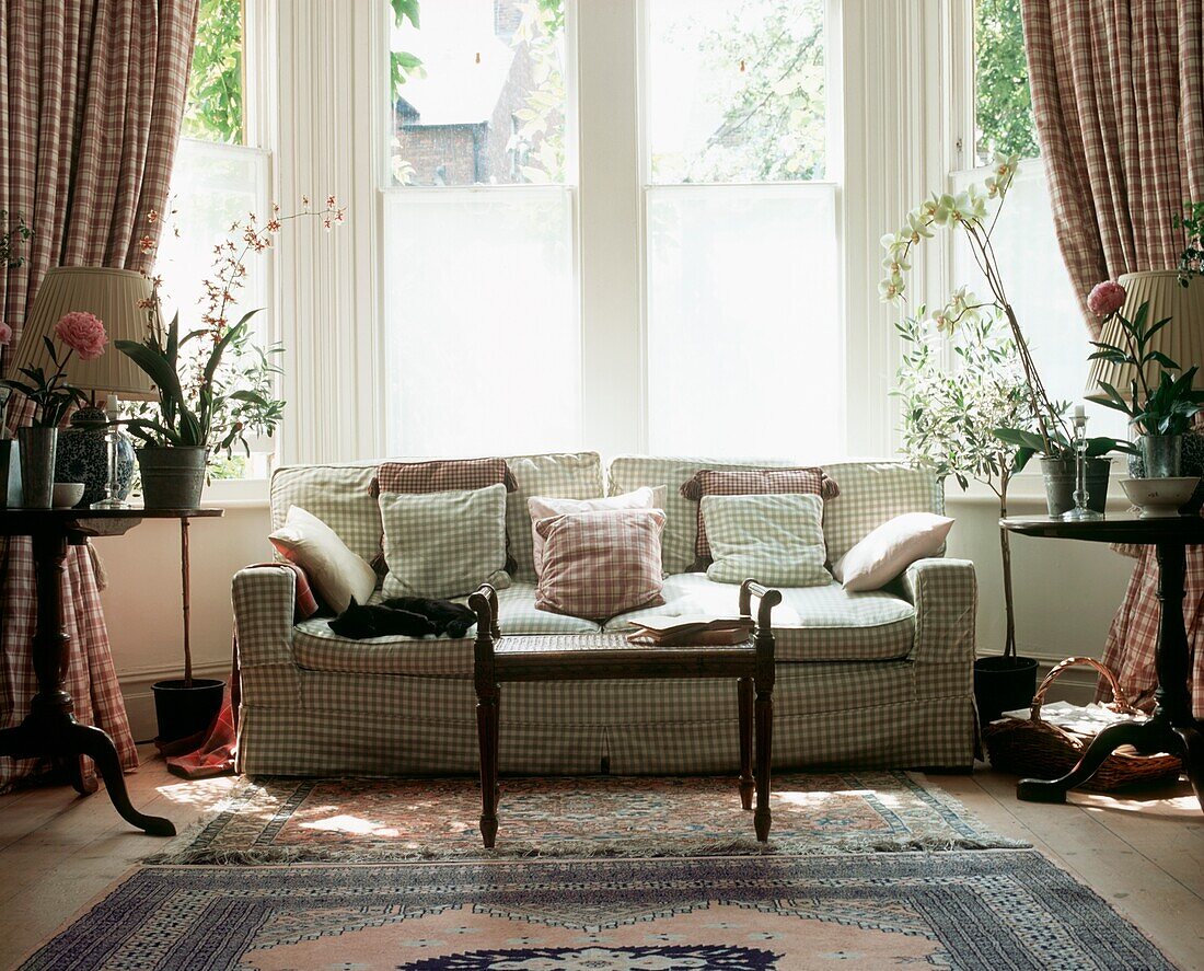 Großes Erkerfenster im Wohnzimmer mit kariertem Sofa und Blumenschmuck