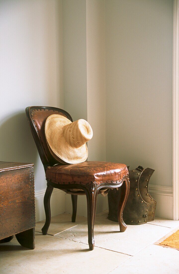 Still life of leather antique chair and straw hat in entrance hall