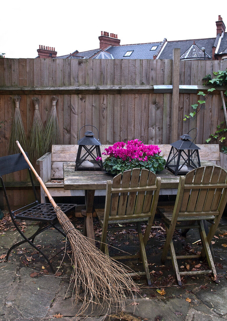 Tisch und Stühle im Freien in einem umzäunten Garten mit Laternen und rosa Blumen