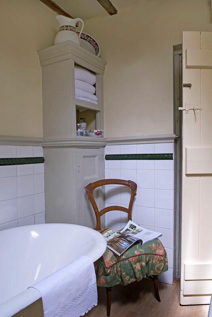 Magazine on chair of bathroom with cabinet and Victorian tiling
