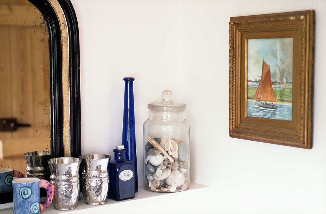 Silberne Pokale und blaues Glas mit Muscheln auf einem Regal im Badezimmer mit nautischem Kunstwerk
