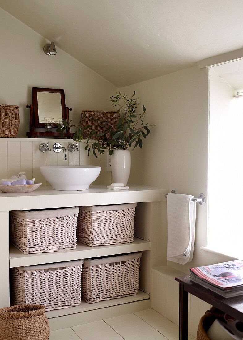 Einbauschrank mit Aufsatzwaschbecken und Aufbewahrungskörben in einem in neutralen Tönen gestrichenen Badezimmer im Dachgeschoss