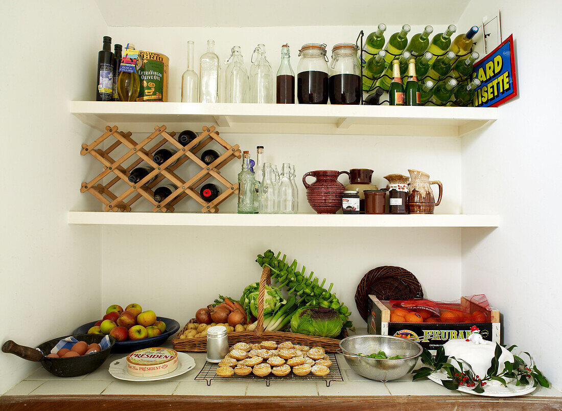Nahaufnahme einer Speisekammer, gefüllt mit Weinflaschen, Hackfleischpasteten, Obst und Gemüse und einem Weihnachtskuchen