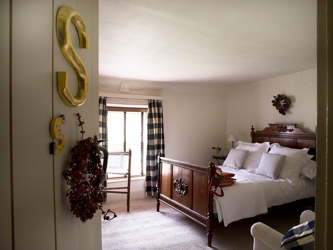 Blick auf ein antikes Mahagoni-Doppelbett durch eine Schlafzimmertür mit Weihnachtskranz und goldenem Buchstaben S