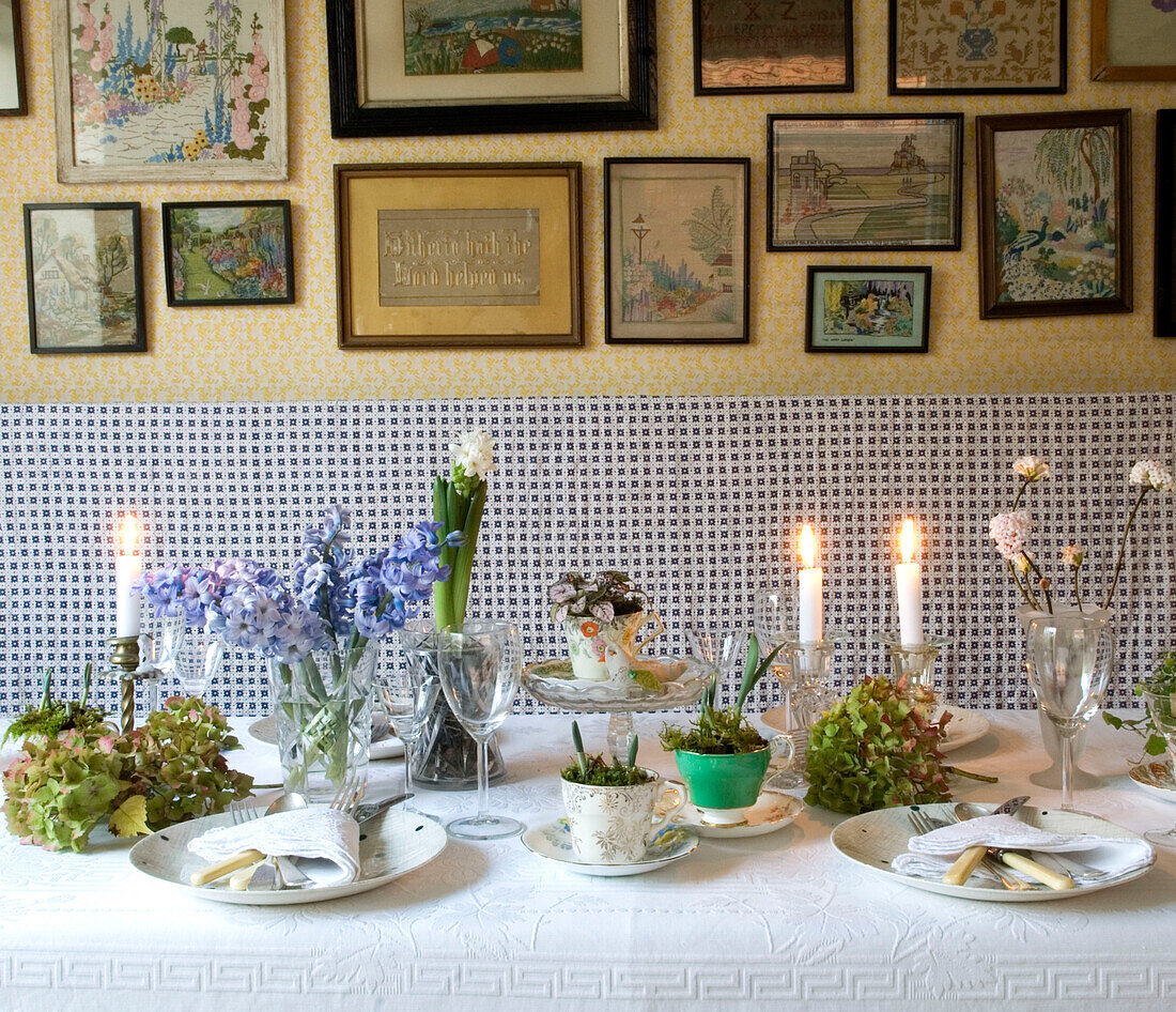 Hübsch gedeckter Tisch mit Kerzen, Hyazinthen- und Blumenzwiebel-Tischdekoration und alten Mustertüchern an der Wand