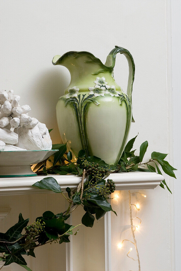 Berried ivy garland draped across the mantlepiece with large green ewer and fairy lights