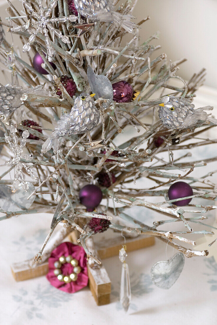 Nahaufnahme eines Weihnachtsbaumständers aus besprühten Zweigen, geschmückt mit silbernen Vögeln und Christbaumkugeln