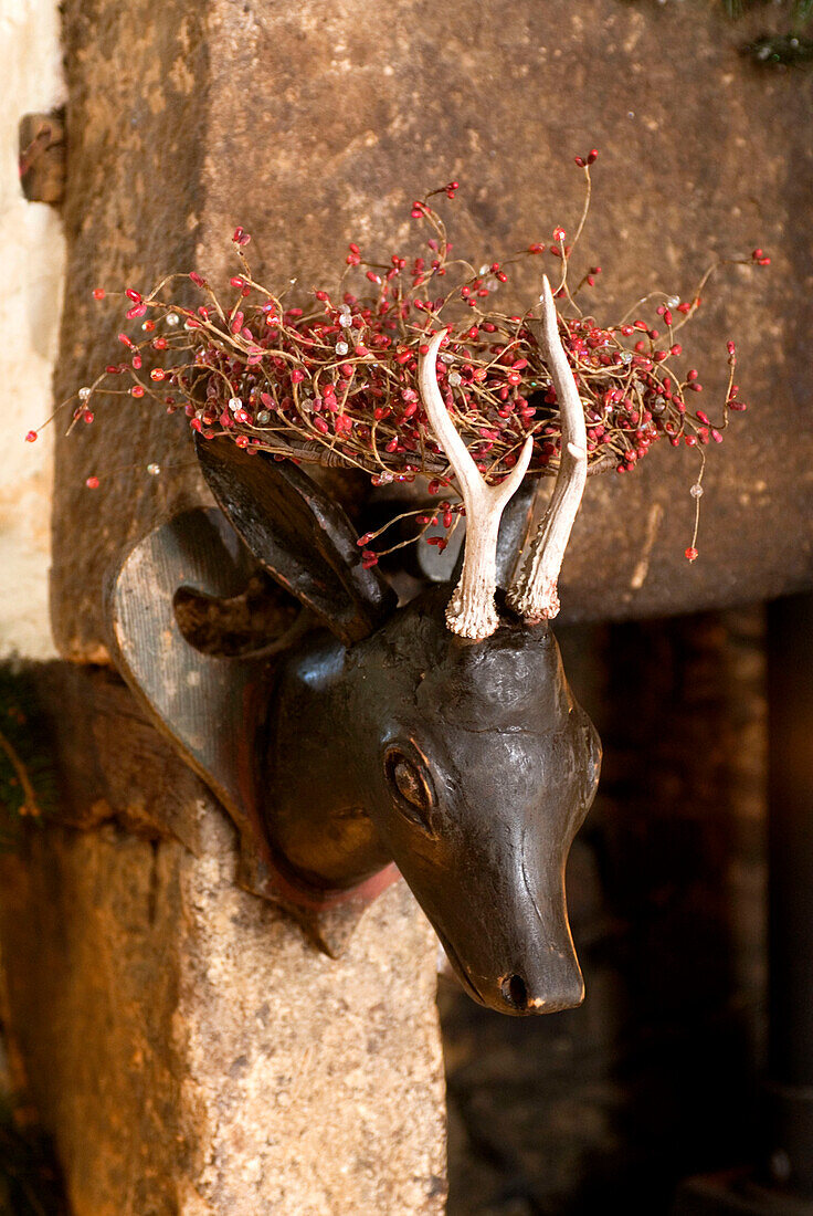 Steinkamin mit an der Wand befestigtem, geschnitztem Hirschkopf und Weihnachtsschmuck aus roten Beeren