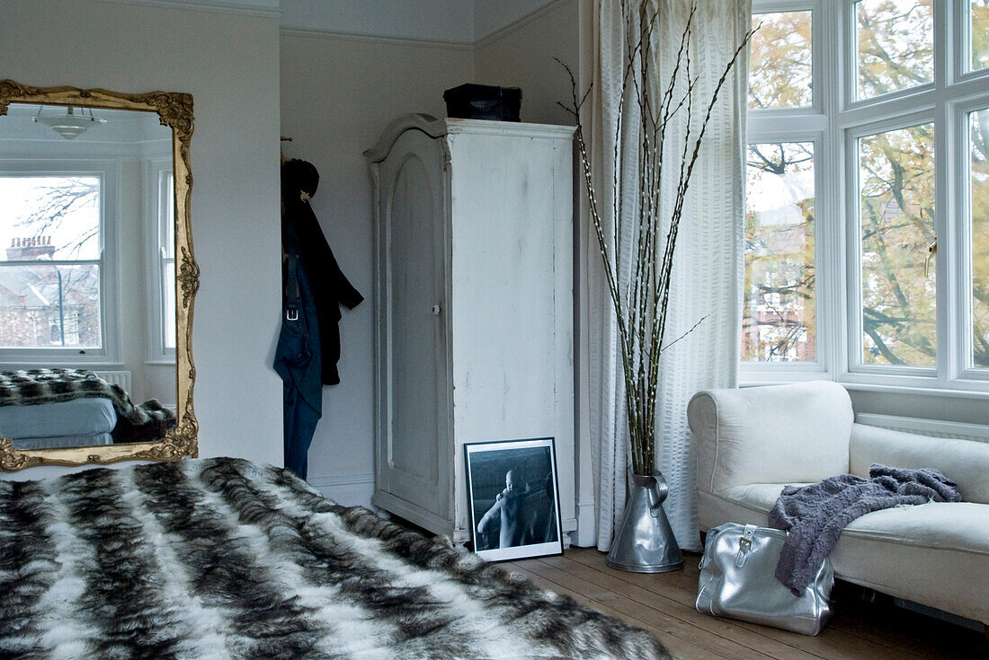 Fur bed cover in room with distressed wardrobe and gilt-framed mirror