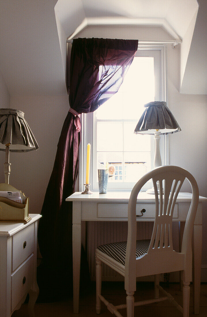 Schreibtisch und Lampe in einer Fensternische mit dunkelrotem, ungefüttertem Seidenvorhang