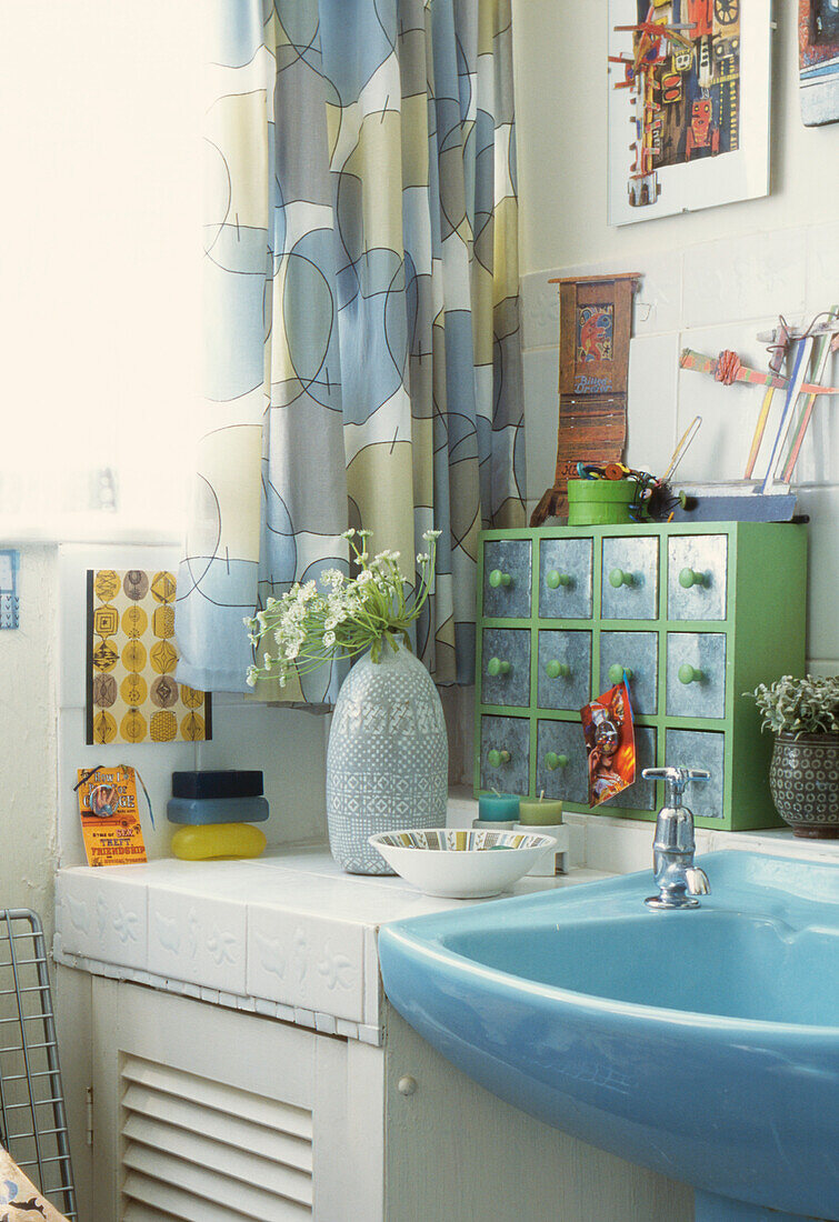 Blassblaue Badezimmereinrichtung mit gebrauchten Vorhängen und einer grünen Miniaturkommode mit verzinkten Metallfronten