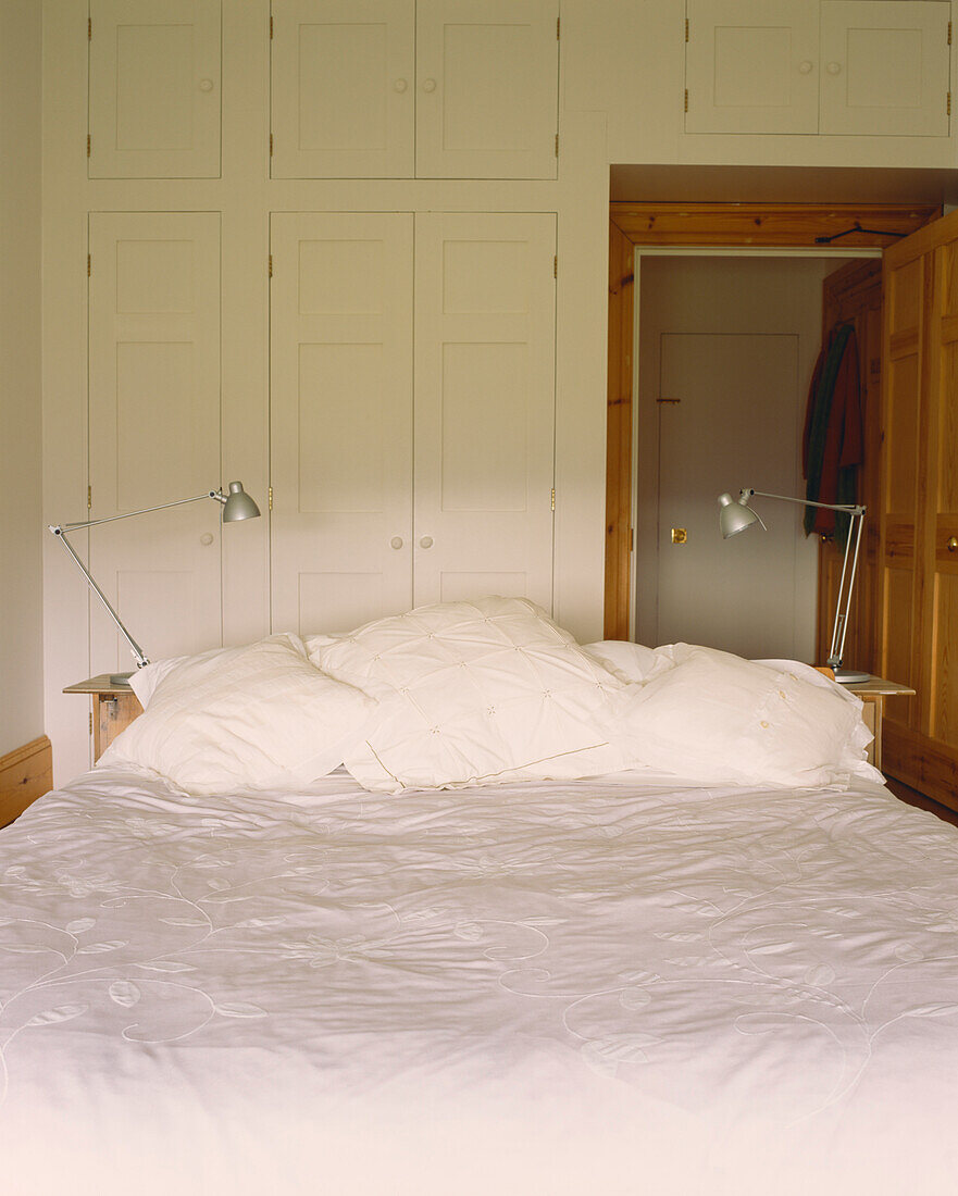 Bett mit weißer Bettwäsche und Winkellampen Einbauschränke und offene Tür