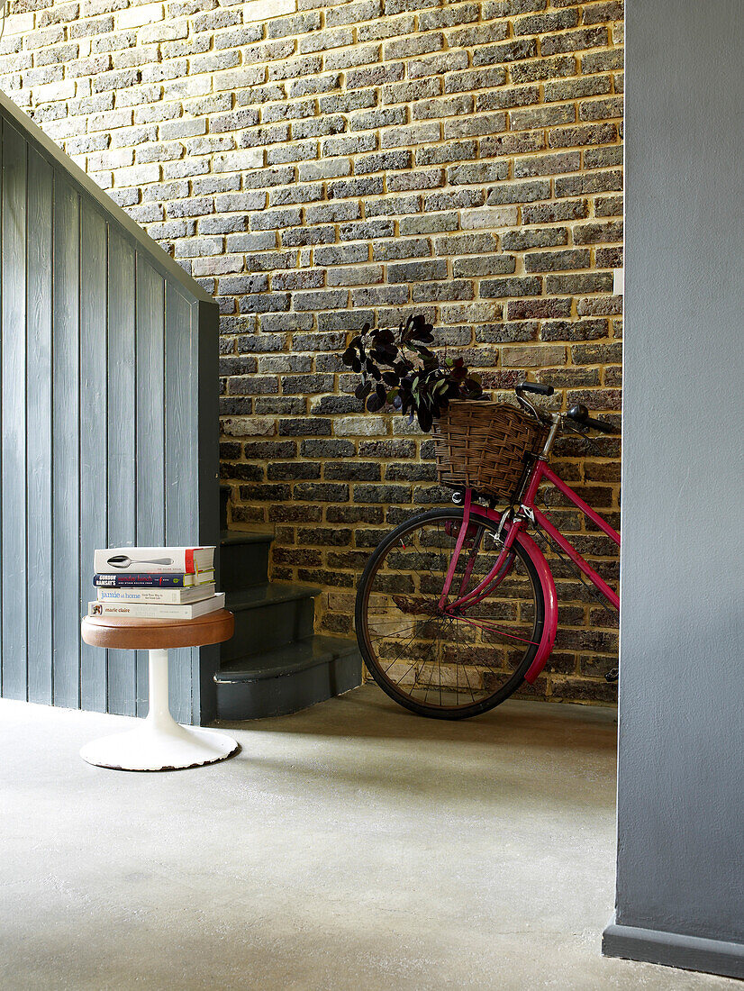 Pink bicycle with basket leaning on exposed brick wall in hallway