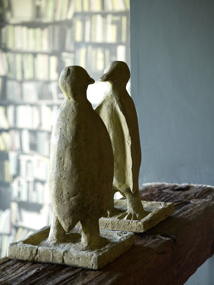 Zwei Pinguin-Skulpturen auf einem Holzregal