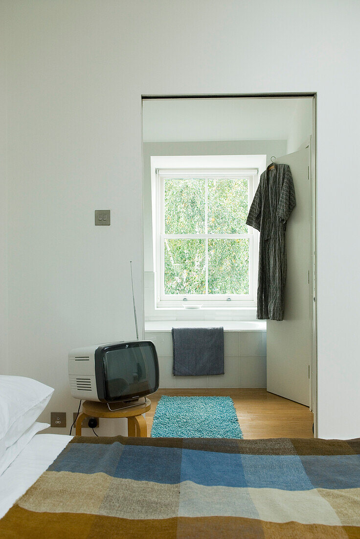 Morgenmantel hängt an der Tür eines sonnenbeschienenen Schlafzimmers mit Fernseher