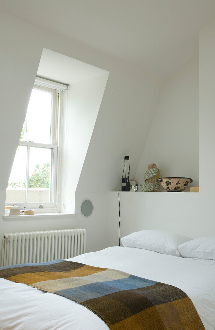 White bedroom with dormer window and folded patterned blanket
