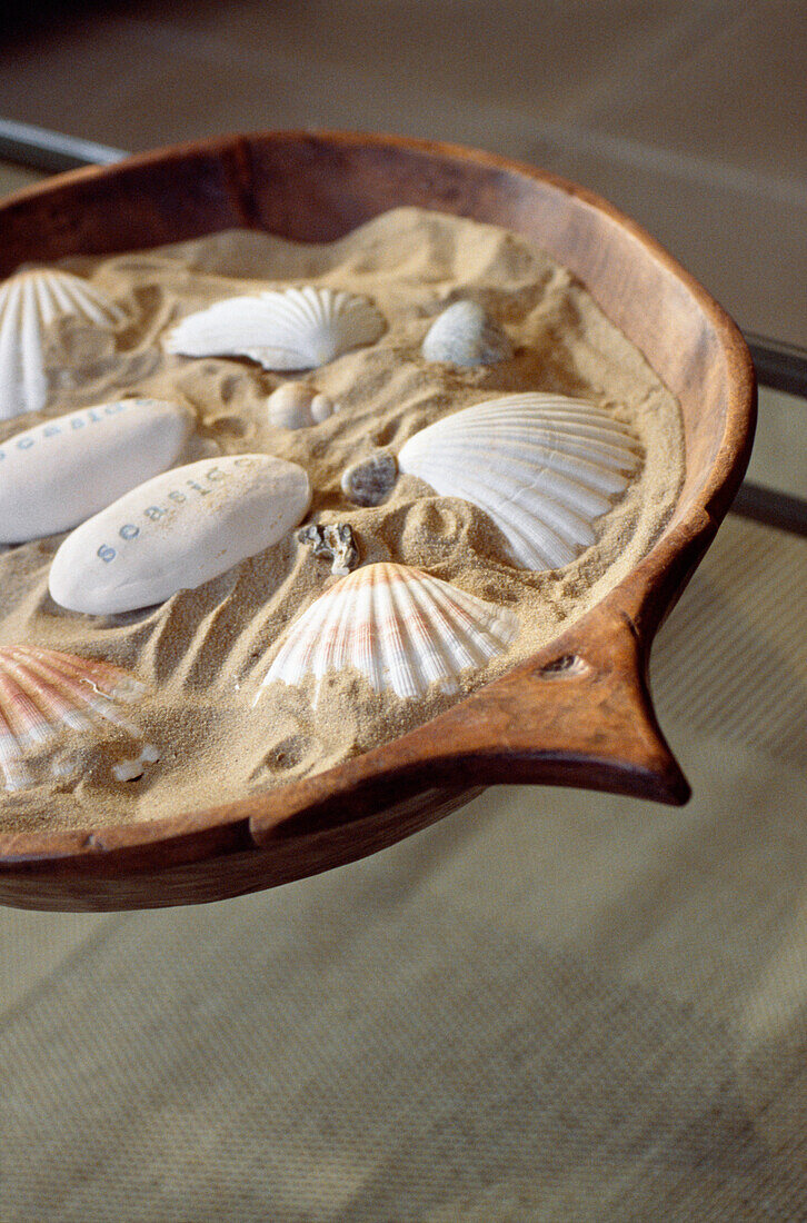Muscheln und beschriftete Kieselsteine in einer mit Sand gefüllten Schale