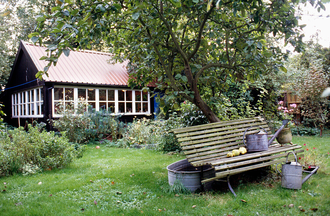 Watering can and tin bath in summerhouse garden with apple tree