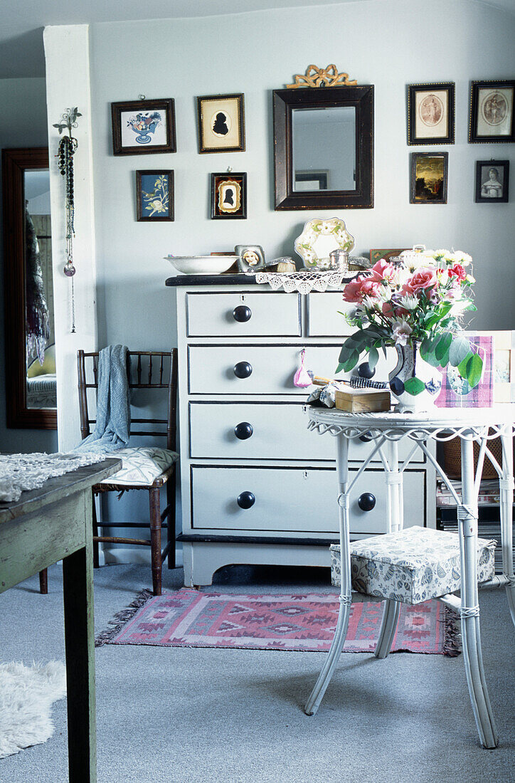 Cameos and artwork with mirror above painted chest of drawers in cottage bedroom