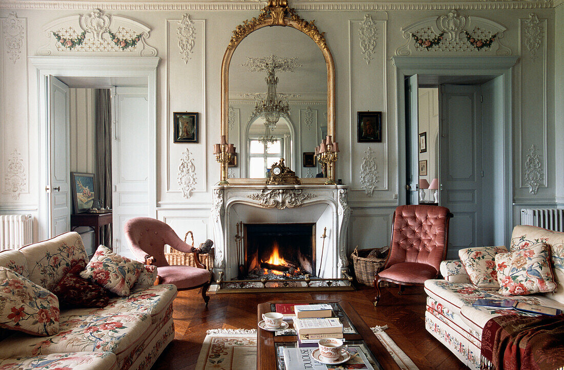 Gilt framed mirror on fireplace in French apartment with floral patterned and pink seating