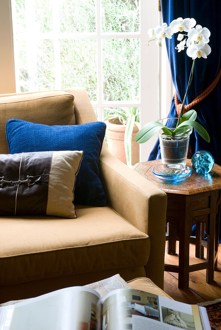 Detail von Sessel mit Kissen und Beistelltisch am Fenster mit weißer Orchidee